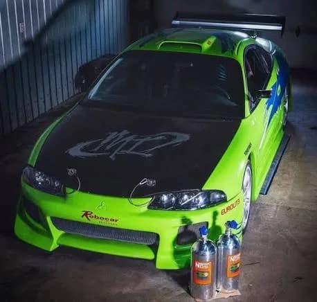 Bright green modified Mitsubishi Eclipse parked in a garage with two polished NOS nitrous oxide bottles resting in front of the bumper.